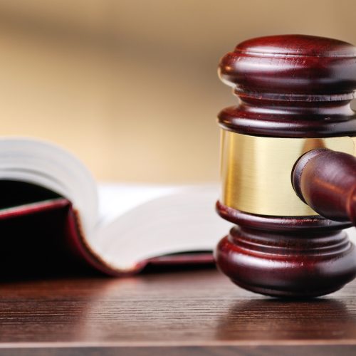 Judges wooden gavel with a brass band around the mallet standing upright on a wooden counter top alongside a law book conceptual of judgements and law enforcement